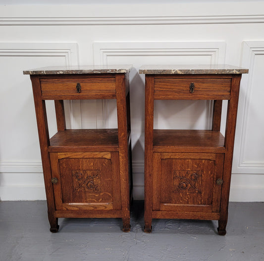Pair of French Oak Arts & Crafts style marble top bedside cabinets. They have lovely carvings on the door, an open shelf in the middle and drawer at the top. They are in good original detailed condition.