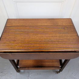 Oak drop leaf auto trolley on wheels. Both sides open up to make a larger table. It is in good original detailed condition.