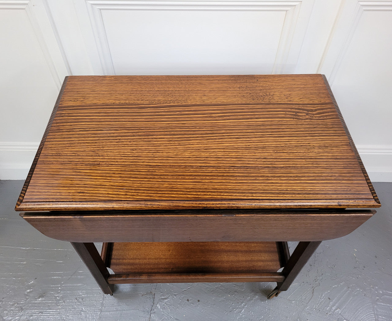 Oak drop leaf auto trolley on wheels. Both sides open up to make a larger table. It is in good original detailed condition.