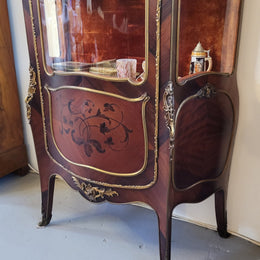 French Louis XV style marquetry inlaid vitrine with ormolu mounts and curved glass. The inside in lined with a red velvet upholstery and has two glass shelves. It has been sourced from France and is in good original detailed condition.