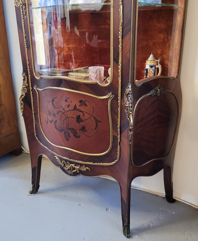 French Louis XV style marquetry inlaid vitrine with ormolu mounts and curved glass. The inside in lined with a red velvet upholstery and has two glass shelves. It has been sourced from France and is in good original detailed condition.