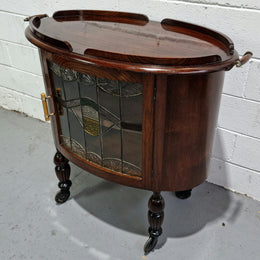 Oak Tudor auto trolley with beautiful leadlight glass. It is on wheels and the door open up to a cabinet with one shelf. In good original detailed condition.