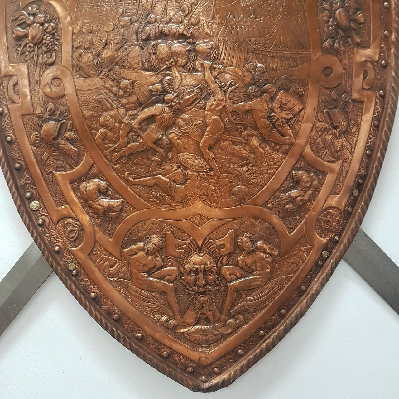 A beautiful European Antique highly detailed embossed copper shield with swords. Look closely to see the amazing detail in the shield of a fighting scene. It has brass handles on the steel swords. Is in good original condition with a slight crack (see photo).