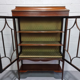 Edwardian Sheraton Revival Mahogany display cabinet with green upholstered  fabric backing and shelving with inlay and two decorative glazed doors.