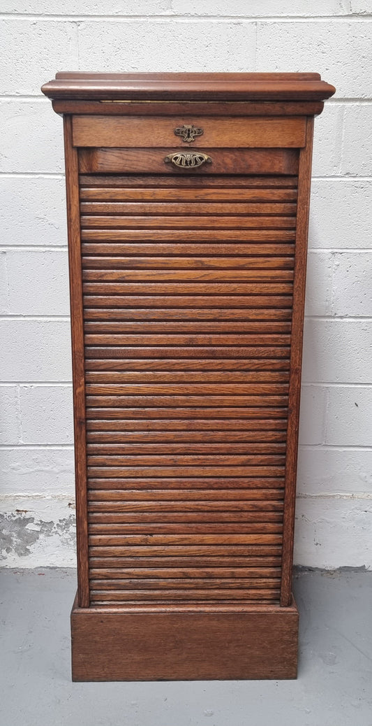 Antique Edwardian roll top Tambour file cabinet desk. This practical antique tambour front filing cabinet dates around 1900 in the Edwardian period and is constructed from Oak. This antique cabinet has an adjustable writing slope, above a tambour front with key and working lock. It has been sourced locally and is in good original detailed condition.
