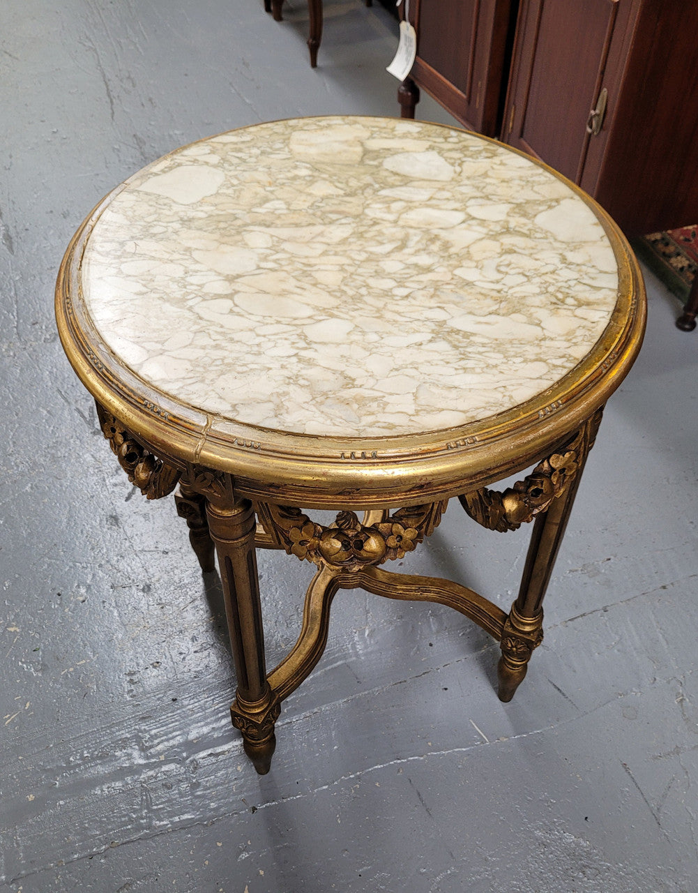 French Louis XVI style round marble topped gilded lamp/side table featuring lovely carved swags and undercarriage. It has been sourced from France and is in good original detailed condition.