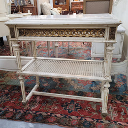 A fabulous painted French Louis XVI style white marble top console table. It has lovely carved detail with gilt highlights and a cane shelf. It has been sourced from France and is in good original condition.
