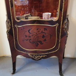 French Louis XV style marquetry inlaid vitrine with ormolu mounts and curved glass. The inside in lined with a red velvet upholstery and has two glass shelves. It has been sourced from France and is in good original detailed condition.