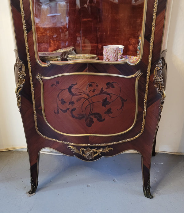 French Louis XV style marquetry inlaid vitrine with ormolu mounts and curved glass. The inside in lined with a red velvet upholstery and has two glass shelves. It has been sourced from France and is in good original detailed condition.