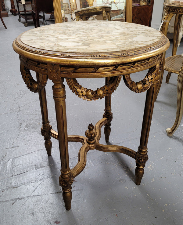 French Louis XVI style round marble topped gilded lamp/side table featuring lovely carved swags and undercarriage. It has been sourced from France and is in good original detailed condition.
