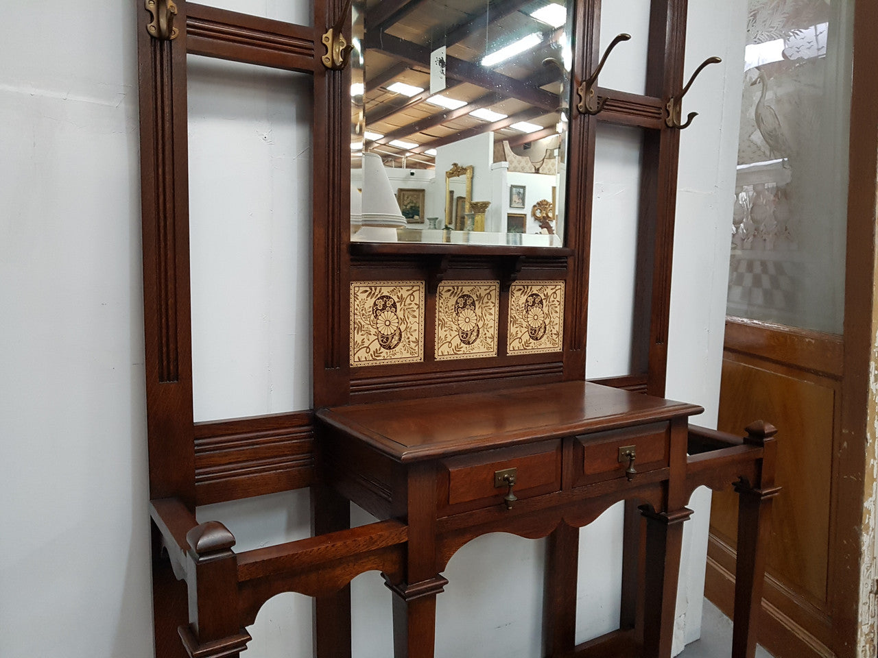 Beautiful English Edwardian tiled back hall stand, with nine brass hooks, two small drawers and retaining it's original mirror and showing signs of age. In good original condition.