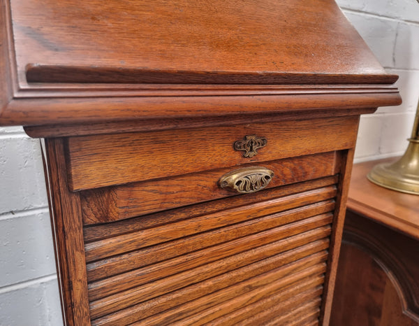 Antique Edwardian roll top Tambour file cabinet desk. This practical antique tambour front filing cabinet dates around 1900 in the Edwardian period and is constructed from Oak. This antique cabinet has an adjustable writing slope, above a tambour front with key and working lock. It has been sourced locally and is in good original detailed condition.