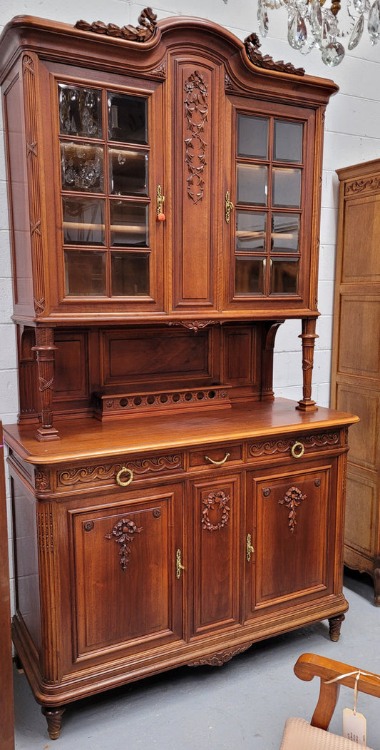 French louis XVI style Walnut buffet hutch featuring bevelled glass in upper doors and carved garlands. Plenty of storage with two drawers four cupboards with one fixed and two adjustable shelves. It has been sourced from France and is in good original detailed condition.