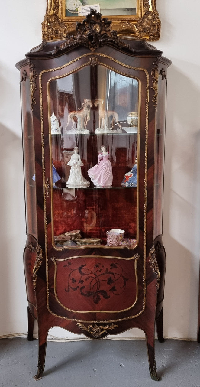 French Louis XV style marquetry inlaid vitrine with ormolu mounts and curved glass. The inside in lined with a red velvet upholstery and has two glass shelves. It has been sourced from France and is in good original detailed condition.