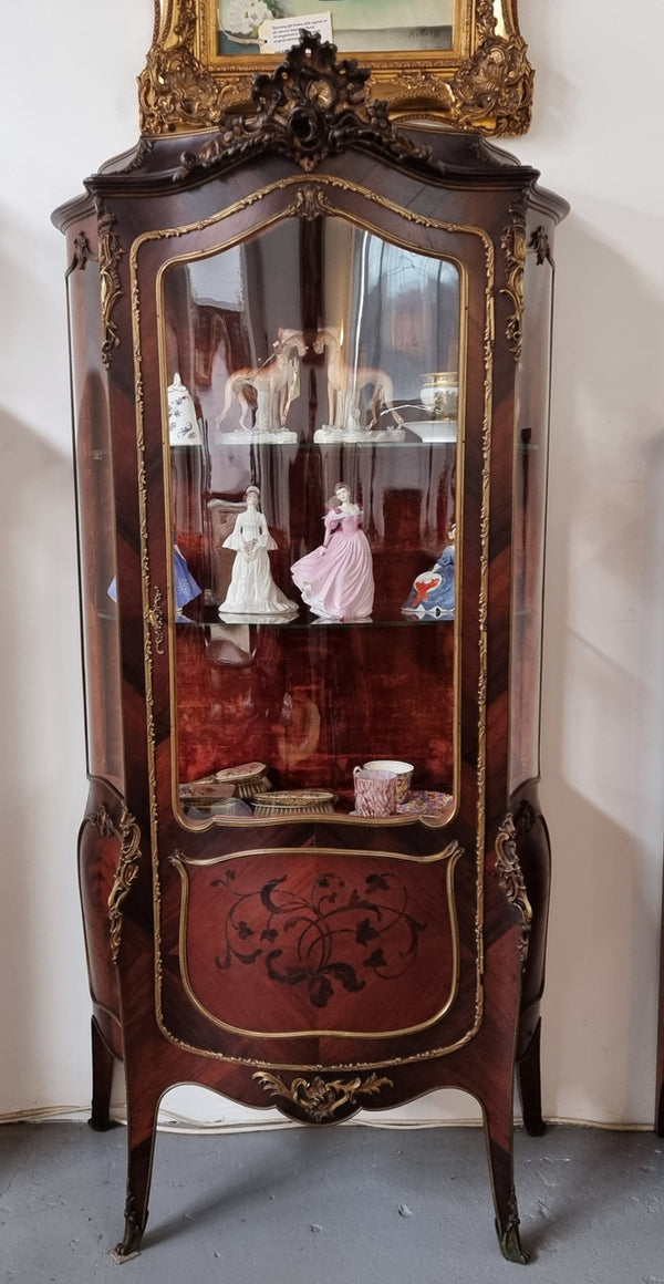 French Louis XV style marquetry inlaid vitrine with ormolu mounts and curved glass. The inside in lined with a red velvet upholstery and has two glass shelves. It has been sourced from France and is in good original detailed condition.
