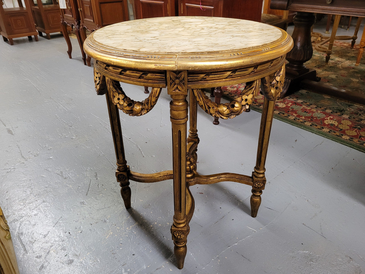 French Louis XVI style round marble topped gilded lamp/side table featuring lovely carved swags and undercarriage. It has been sourced from France and is in good original detailed condition.