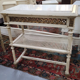A fabulous painted French Louis XVI style white marble top console table. It has lovely carved detail with gilt highlights and a cane shelf. It has been sourced from France and is in good original condition.