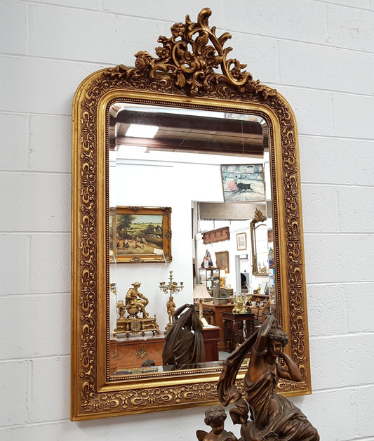 19th Century French Louis XV style gilt wall mirror with fabulous highly decorative crest at the top and a beveled edge mirror. In good original detailed condition.