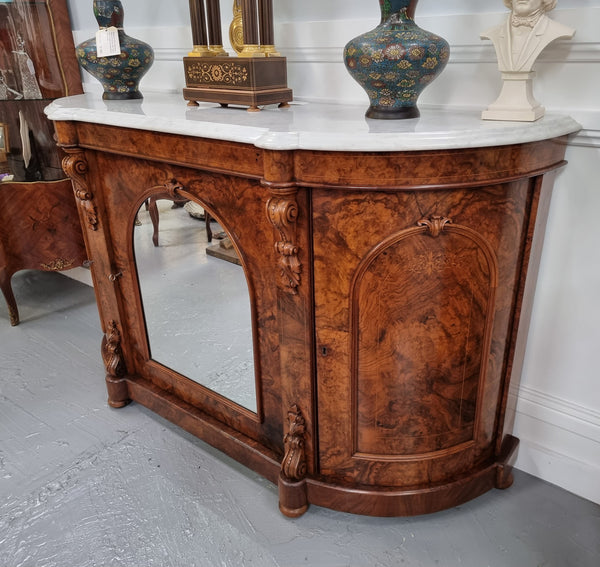 An elegant Antique Victorian Burr wood Walnut marble-top sideboard credenza with a mirrored center door. It has a white shaped marble top, mirror front, nicely carved details and three swing doors along with two keys. It is in good original detailed condition.