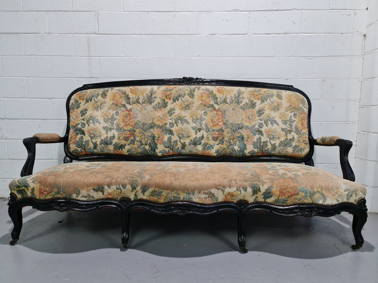 Substantial Antique 19th century Louis XV style ebonized serpentine front settee. The fabric is in used condition showing use and could be used as is or reupholster. Very easily sits three people with space between each person. Also selling separately a pair of matching arm chairs.