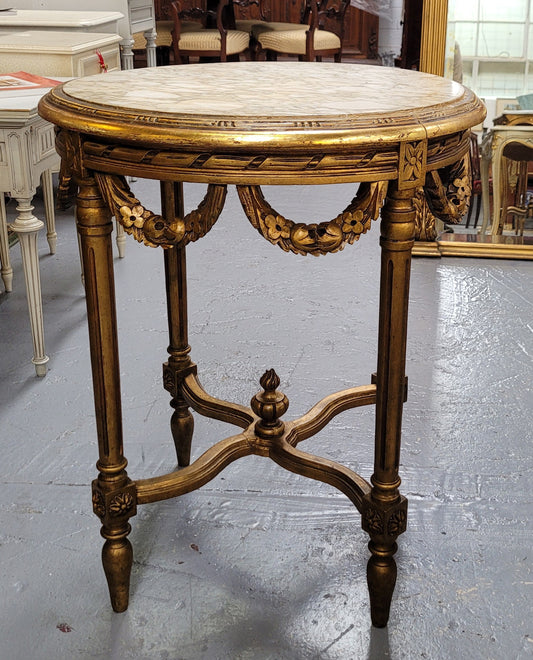 French Louis XVI style round marble topped gilded lamp/side table featuring lovely carved swags and undercarriage. It has been sourced from France and is in good original detailed condition.