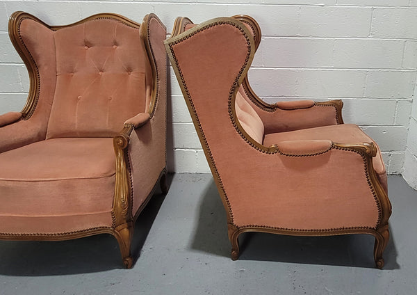 French pair of  Walnut Louis XV style pink upholstered wing back chairs. They are very comfortable to sit in and are of generous portions. The fabric is in good original condition and does have stains and would ideally be reupholstered.