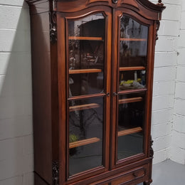 Antique Mahogany two door Biedermeier style bookcase with four fully adjustable shelves and a drawer at the bottom. The two wooden finials at the top are easily removed for a different look of desired. In good original detailed condition.