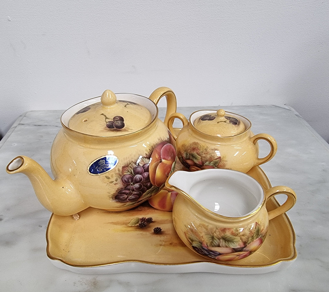 “Aynsley Orchard Gold” tea set on tray. Consisting of small teapot, lidded sugar and creamer. Please view photos as they help form part of the description.