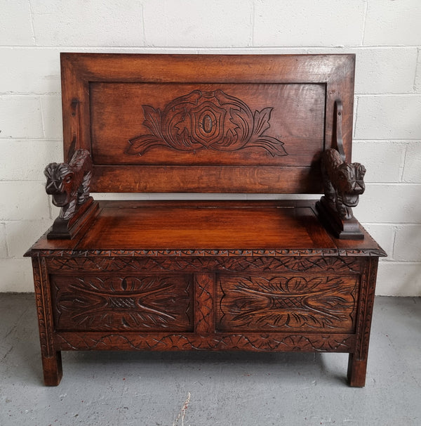 Unusual English Oak Monks Bench.  The tabletop is set onto a lift top chest in such a way that when the table is not in use, the top pivots to a vertical position and becomes the back of a Settle. Carved Lion table rests and carving to front.  In good, detailed condition.