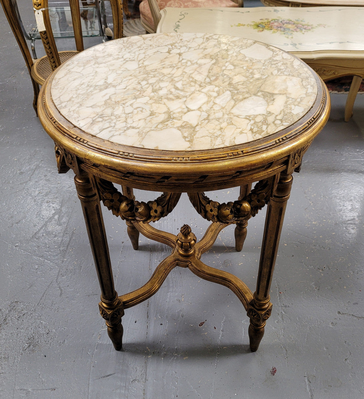 French Louis XVI style round marble topped gilded lamp/side table featuring lovely carved swags and undercarriage. It has been sourced from France and is in good original detailed condition.