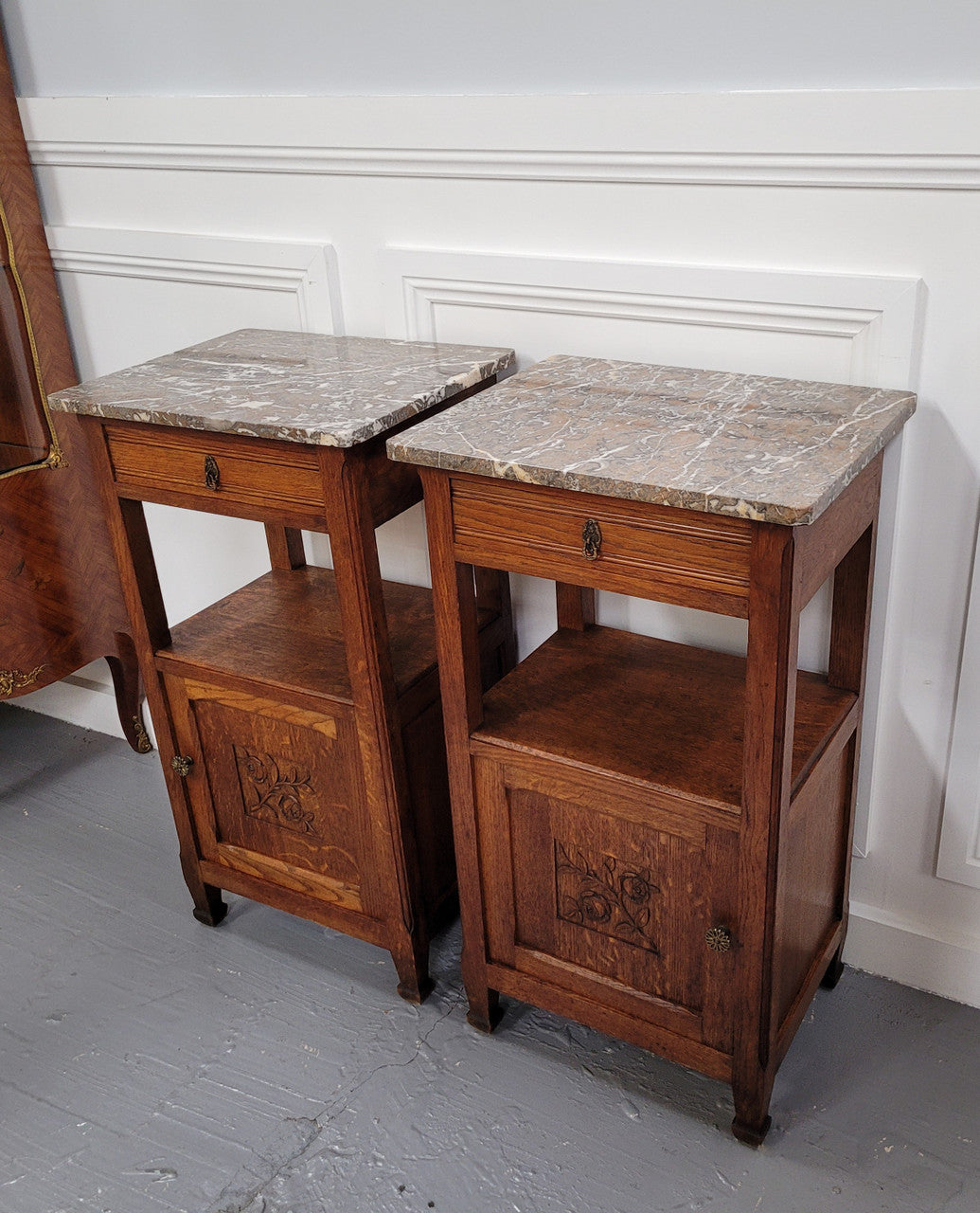 Pair of French Oak Arts & Crafts style marble top bedside cabinets. They have lovely carvings on the door, an open shelf in the middle and drawer at the top. They are in good original detailed condition.