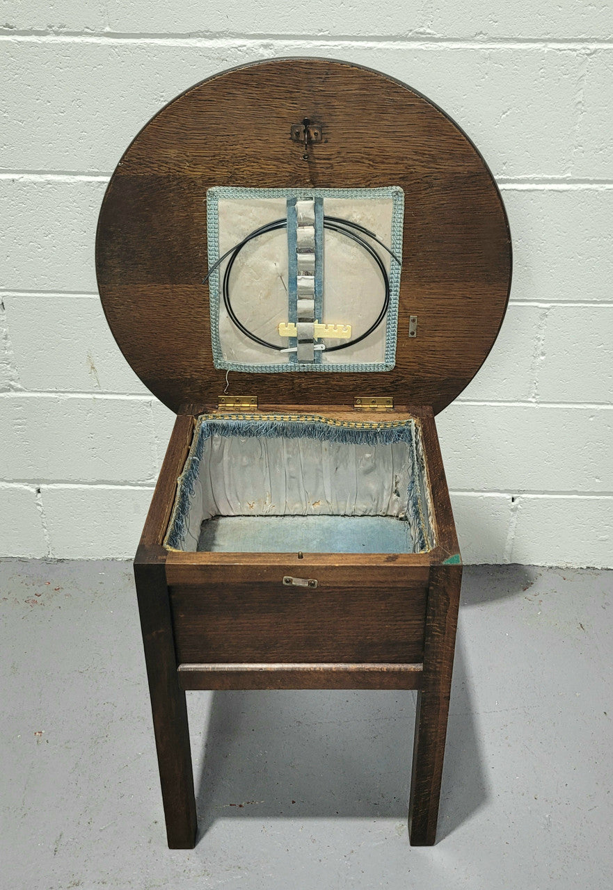 Fabulous round oak side table which also has a hidden sewing box underneath with lovely original blue satin lining and Includes pictured sewing items. It is in good original condition.