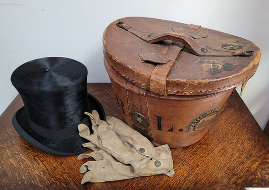 Black Silk Top Hat manufactured by the Buzolich Family, Melbourne between 1910 – 1927 (now City Hatters Flinders Street). Includes original Leather Hat Box with insert for hat. Hat in good condition, box shows wear and deterioration commensurate with age and has part labels from travel affixed.