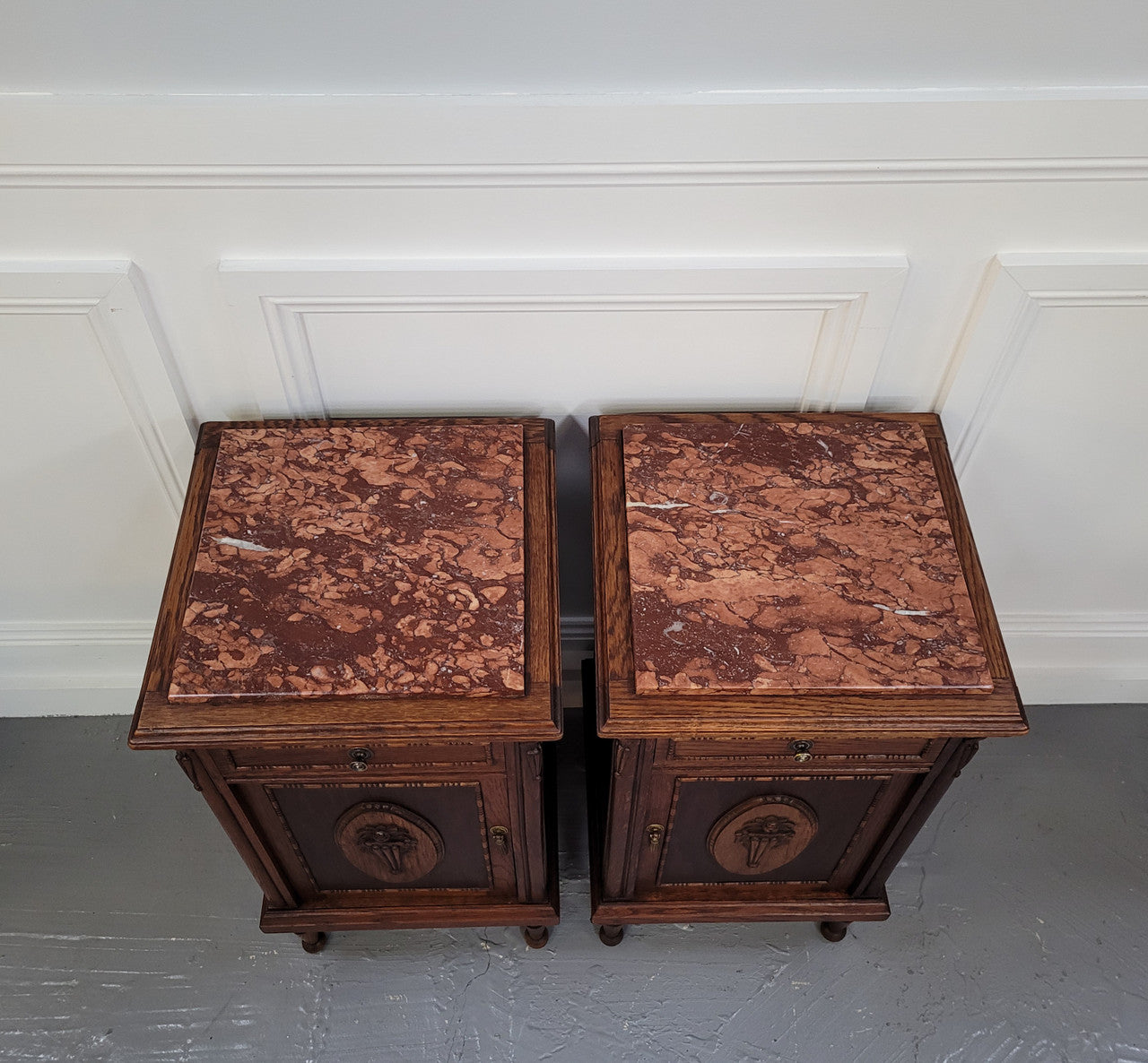 Pair of French Art Deco Oak and rouge inset marble top bedside cabinets. They have one drawer and one cupboard with elegant carving on the door. They have been sourced from France and are in good original detailed condition.