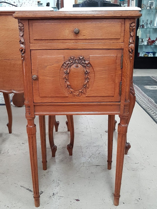 A French oak single bedside cabinet, with a marble inset top, finely carved detail, cupboard space and a drawer. In good original condition.