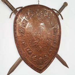A beautiful European antique repousse copper shield, depicting a battle scene and with metal swords. It has been sourced from France and is in good original condition.