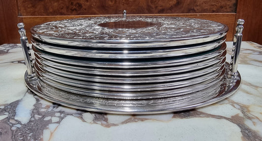 Five Strachan and two Rodd silver plate table coasters in a silver plate stand. In good original detailed condition.