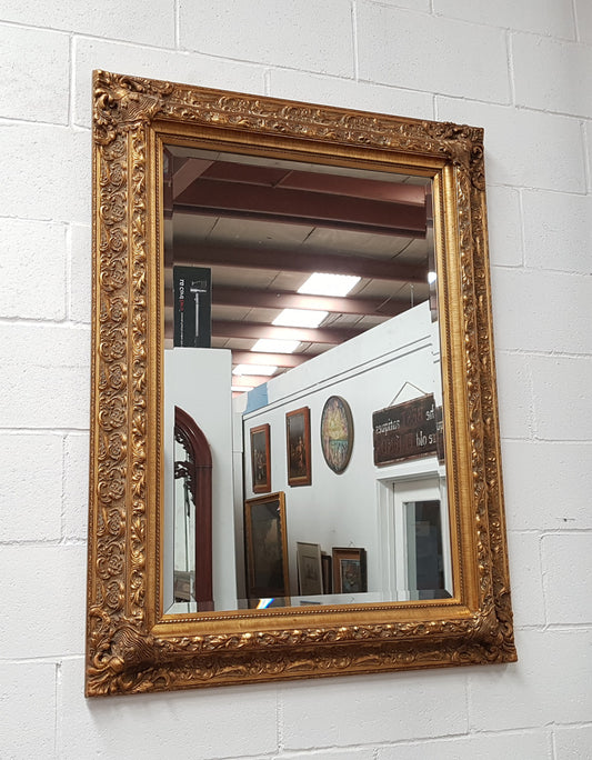A beautiful French style reproduction heavily carved ornate gilt wall mirror in good original condition.