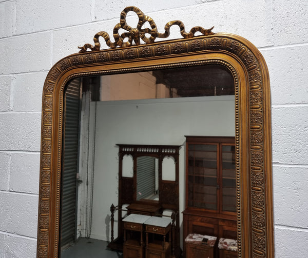Late 19th century French gilt mirror with beautiful ribbon crest on top. In good original detailed condition.