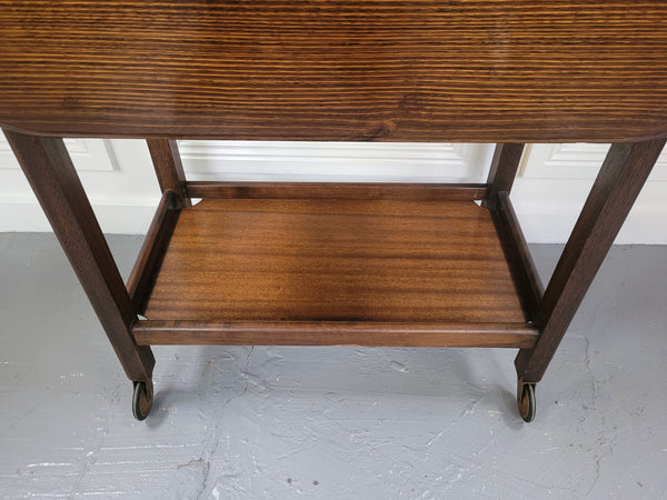Oak drop leaf auto trolley on wheels. Both sides open up to make a larger table. It is in good original detailed condition.