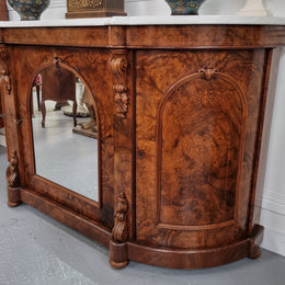 An elegant Antique Victorian Burr wood Walnut marble-top sideboard credenza with a mirrored center door. It has a white shaped marble top, mirror front, nicely carved details and three swing doors along with two keys. It is in good original detailed condition.