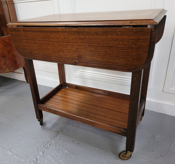 Oak drop leaf auto trolley on wheels. Both sides open up to make a larger table. It is in good original detailed condition.