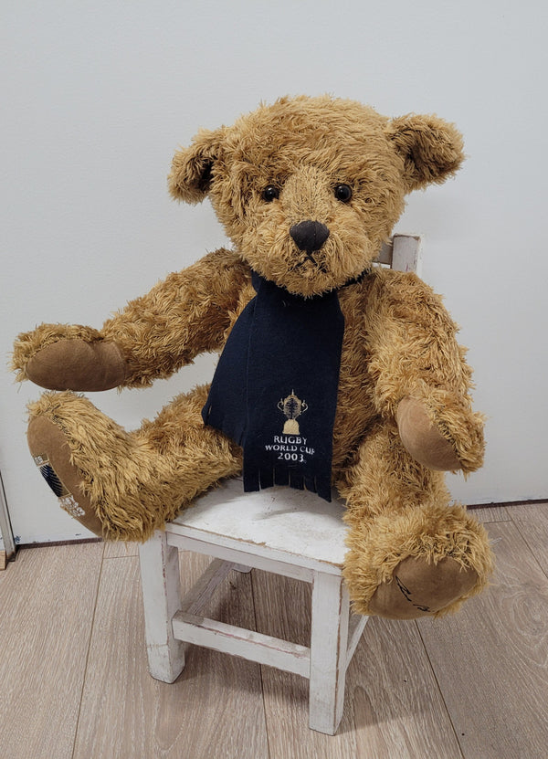 World Cup Rugby Bear. William by RUSS a special release for 2003. Limited to 5000 pieces worldwide. 50.8 cm fully jointed golden-brown bear with suedeen paw pads and blue scarf with Rugby World Cup Logo embroidery.

*Please note chair in photo is not included.