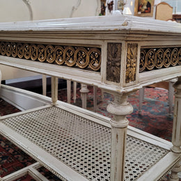 A fabulous painted French Louis XVI style white marble top console table. It has lovely carved detail with gilt highlights and a cane shelf. It has been sourced from France and is in good original condition.