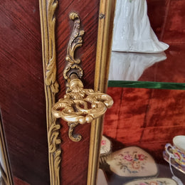 French Louis XV style marquetry inlaid vitrine with ormolu mounts and curved glass. The inside in lined with a red velvet upholstery and has two glass shelves. It has been sourced from France and is in good original detailed condition.