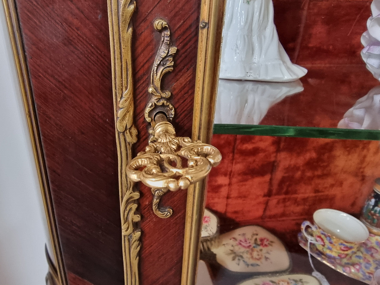 French Louis XV style marquetry inlaid vitrine with ormolu mounts and curved glass. The inside in lined with a red velvet upholstery and has two glass shelves. It has been sourced from France and is in good original detailed condition.