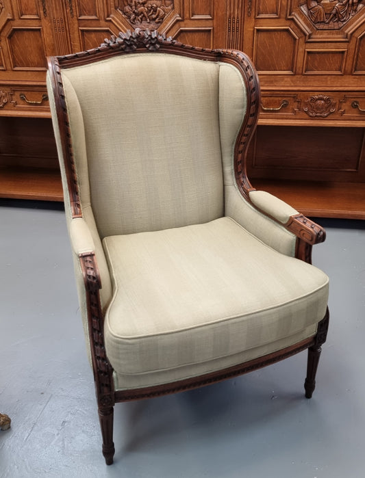 Beautifully carved Louis XVI Walnut upholstered wingback chair. The upholstery is in good original condition with no tears. The chair is also in very good original condition.