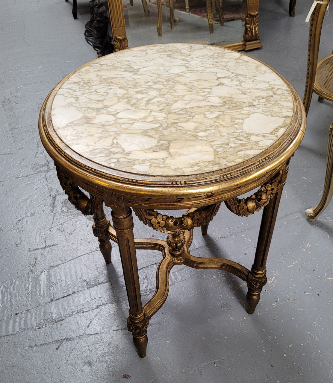 French Louis XVI style round marble topped gilded lamp/side table featuring lovely carved swags and undercarriage. It has been sourced from France and is in good original detailed condition.