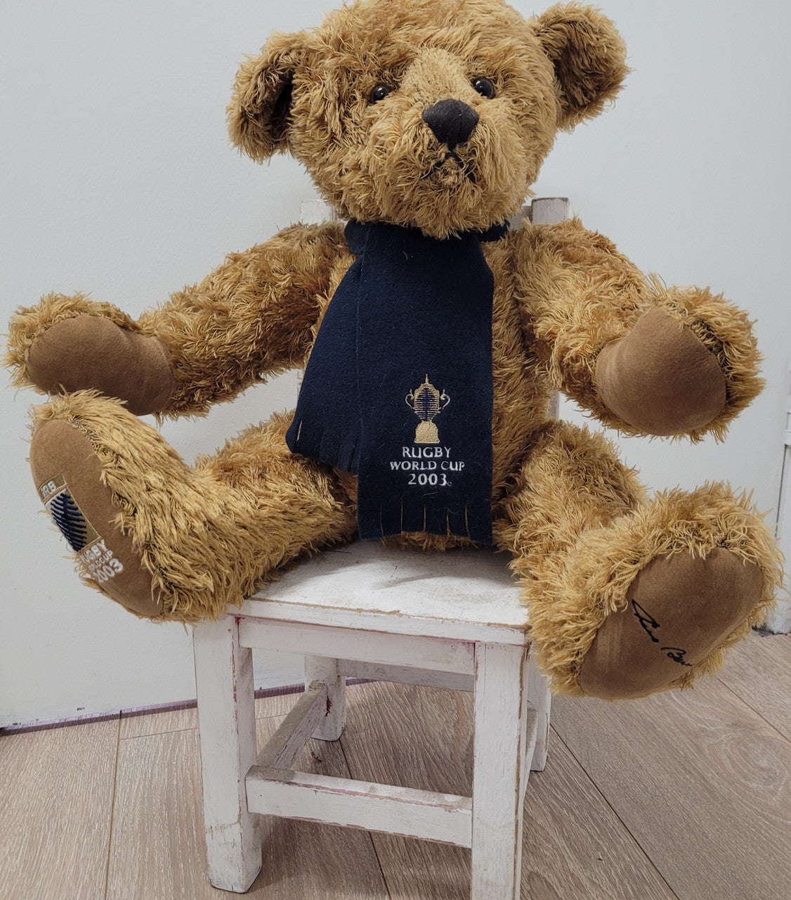 World Cup Rugby Bear. William by RUSS a special release for 2003. Limited to 5000 pieces worldwide. 50.8 cm fully jointed golden-brown bear with suedeen paw pads and blue scarf with Rugby World Cup Logo embroidery.

*Please note chair in photo is not included.