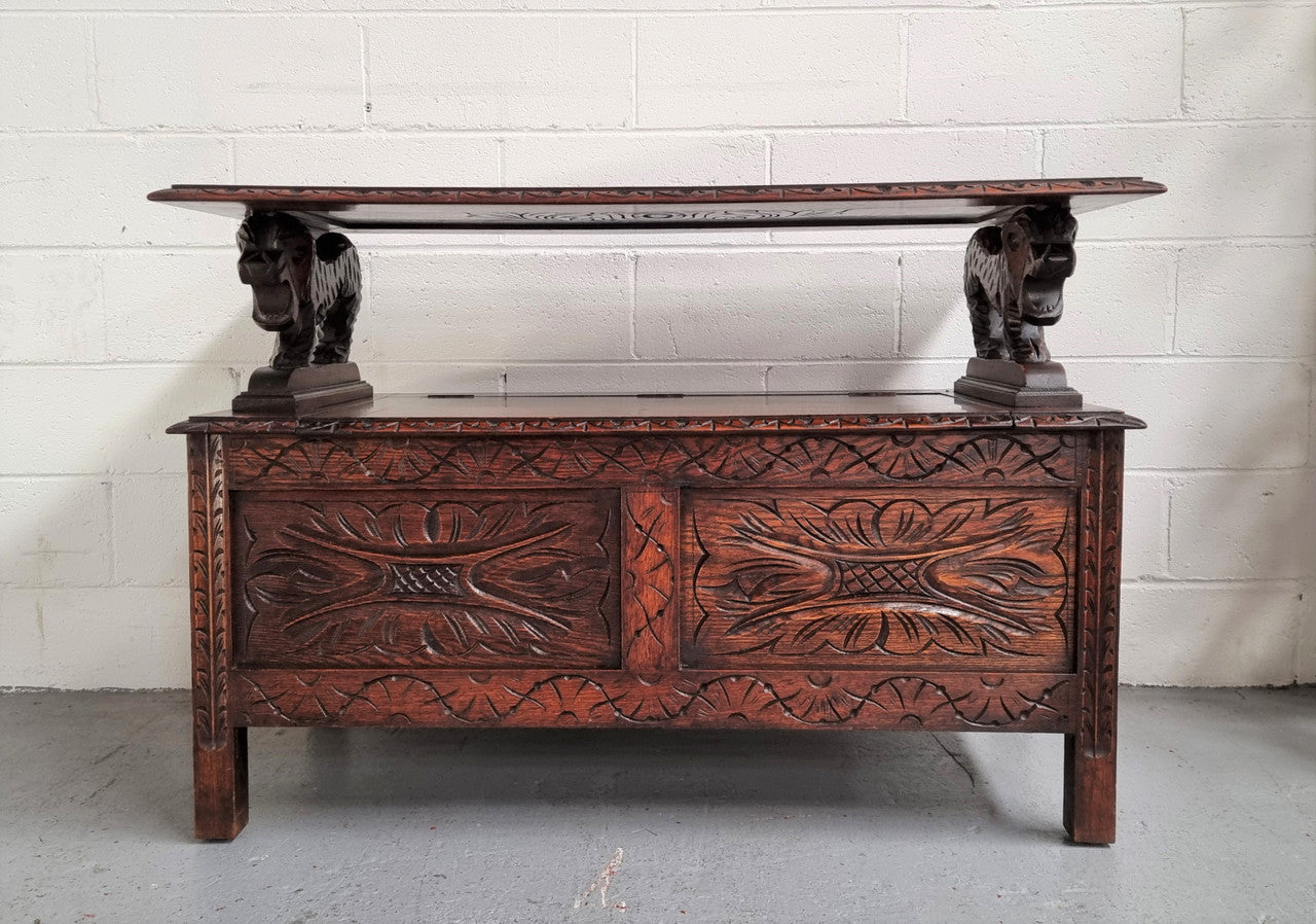 Unusual English Oak Monks Bench.  The tabletop is set onto a lift top chest in such a way that when the table is not in use, the top pivots to a vertical position and becomes the back of a Settle. Carved Lion table rests and carving to front.  In good, detailed condition.